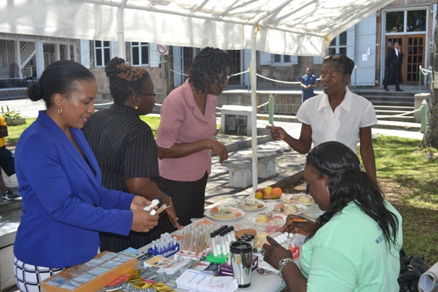 (Left) Permanent Secretary in the Ministry of Health Nicole-Slack Liburd observing the activity at a booth manned by (extreme left) Vernice Blackett, nutritionist at the Alexandra Hospital during the Nevis Health Promotion Unit’s free health screening activity on April 07, 2016, at the War Memorial in Charlestown in observance of World Health Day
